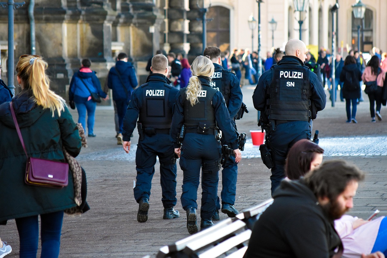 Policjanci w mundurach "POLIZEI" zabezpieczający wydarzenie, przypominający o bezpieczeństwie wojskowym.