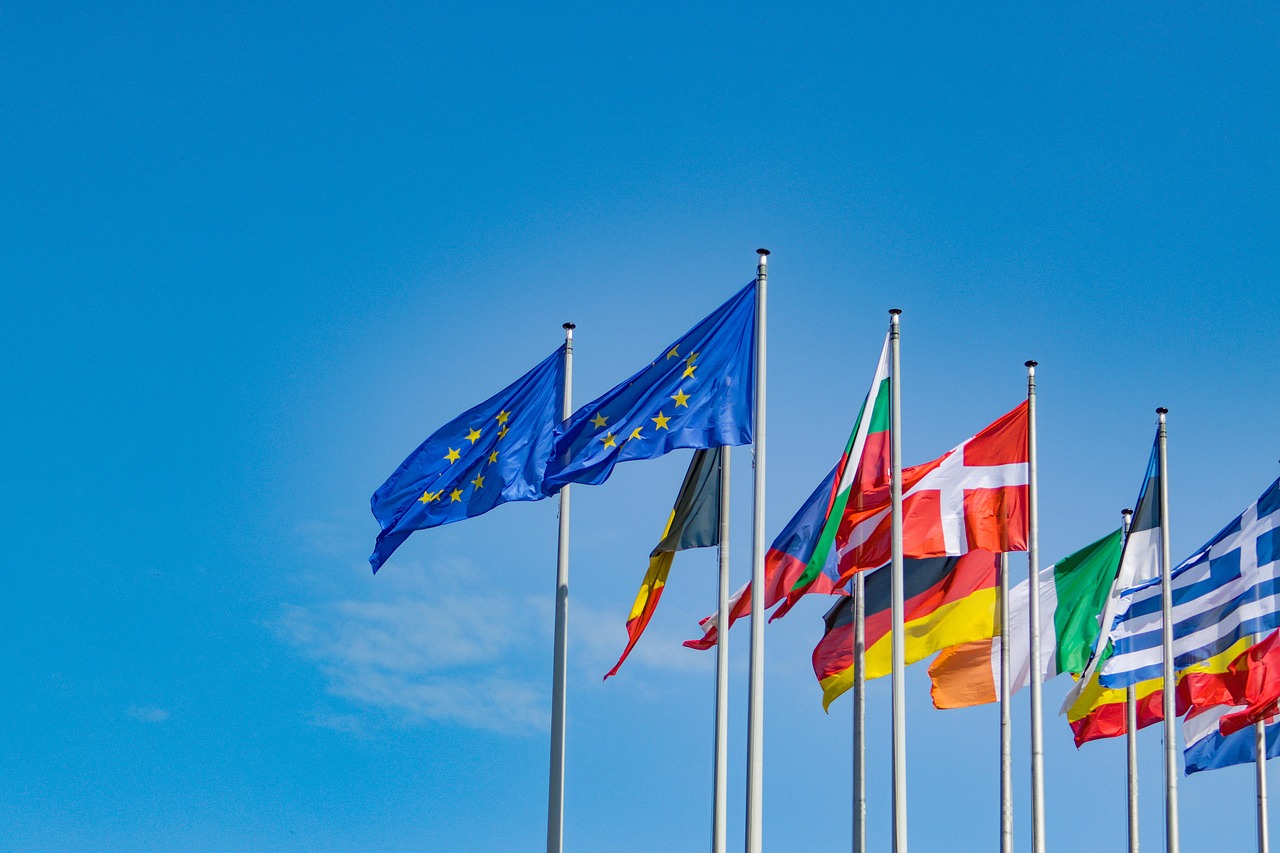 Flagi europejskie na tle błękitnego nieba, symbolizujące polityczne i międzynarodowe aspekty stanowiska w ONZ.