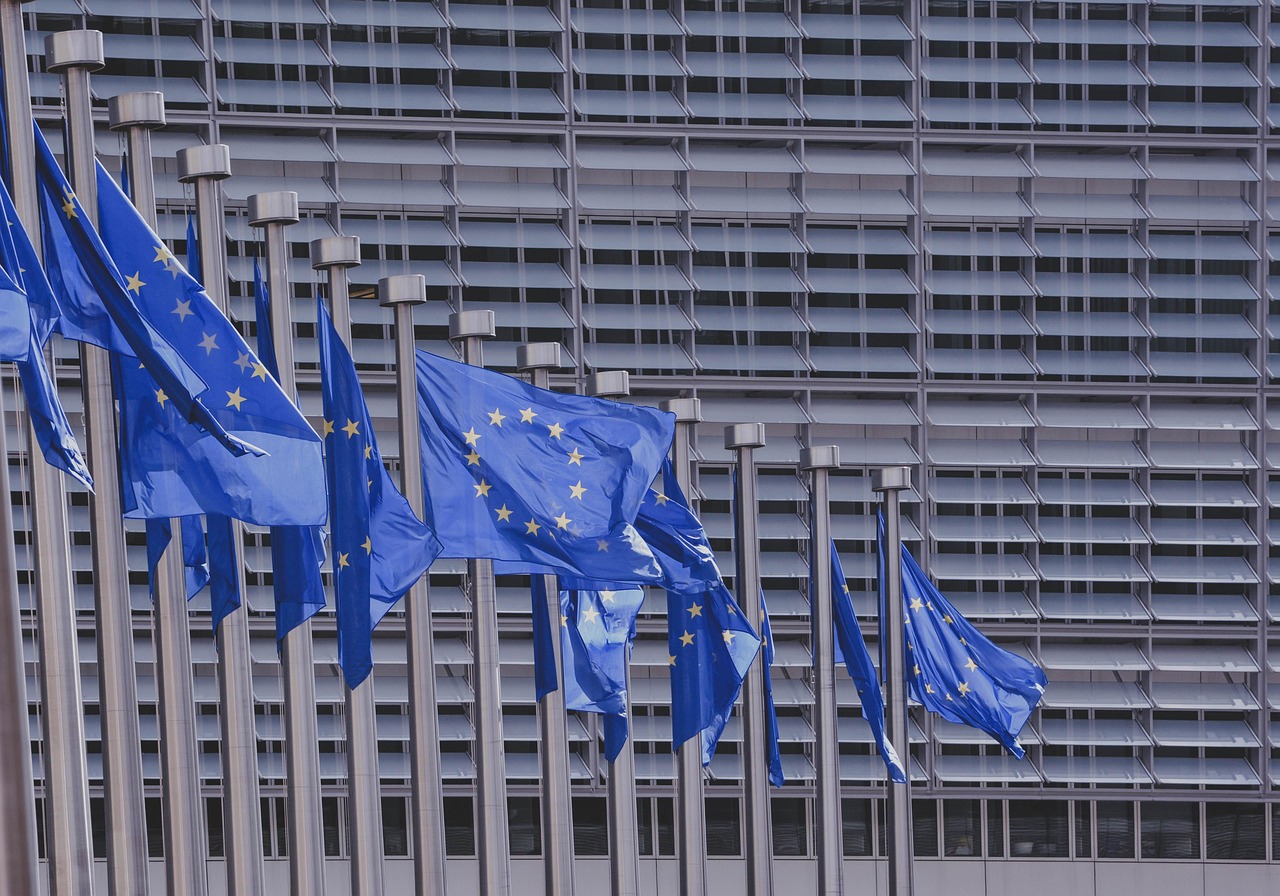 Flagi Unii Europejskiej przed budynkiem Komisji Europejskiej w Brukseli, symbolizujące instytucje UE.