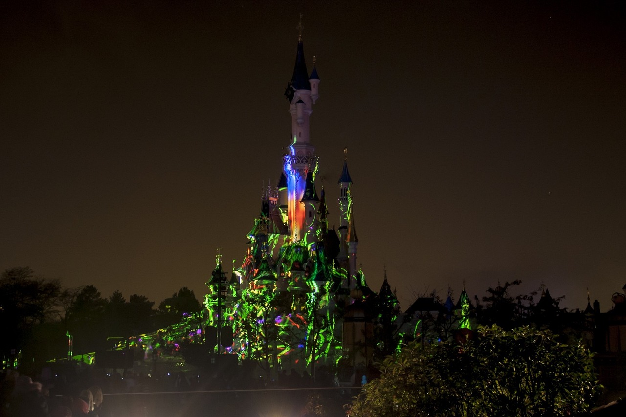 Zamek w Disneylandzie oświetlony kolorowymi projekcjami nocą, nawiązanie do Nawiedzonego Domu.
