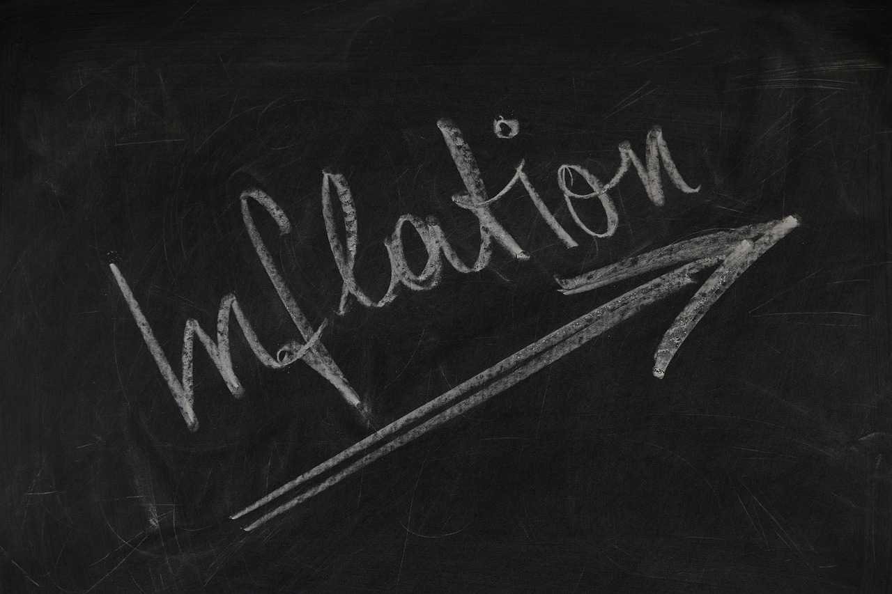 Napis "Inflation" kredą na tablicy z zaznaczoną strzałką w górę, symbolizującą wzrost cen.