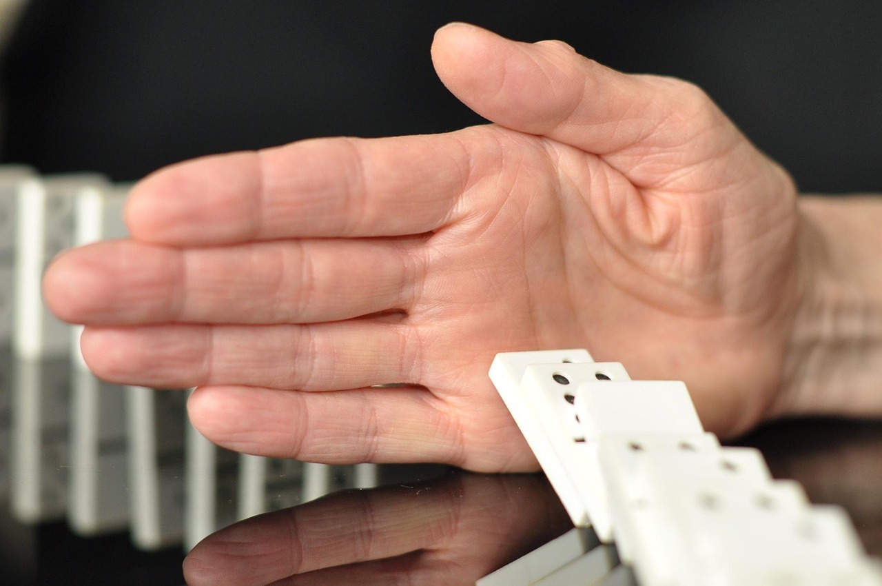 Dłoń powstrzymująca domino symbolizujące spór prawny byłego prezesa Orlenu