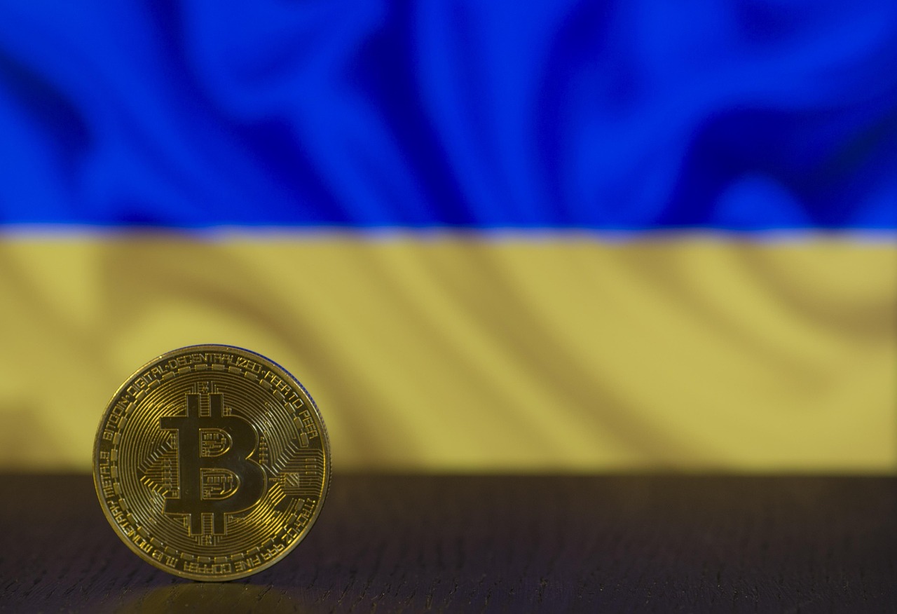 Moneta Bitcoin na tle flagi Ukrainy, symbolizująca potencjalne wsparcie finansowe lub ekonomiczne w obliczu ataków na energetykę.