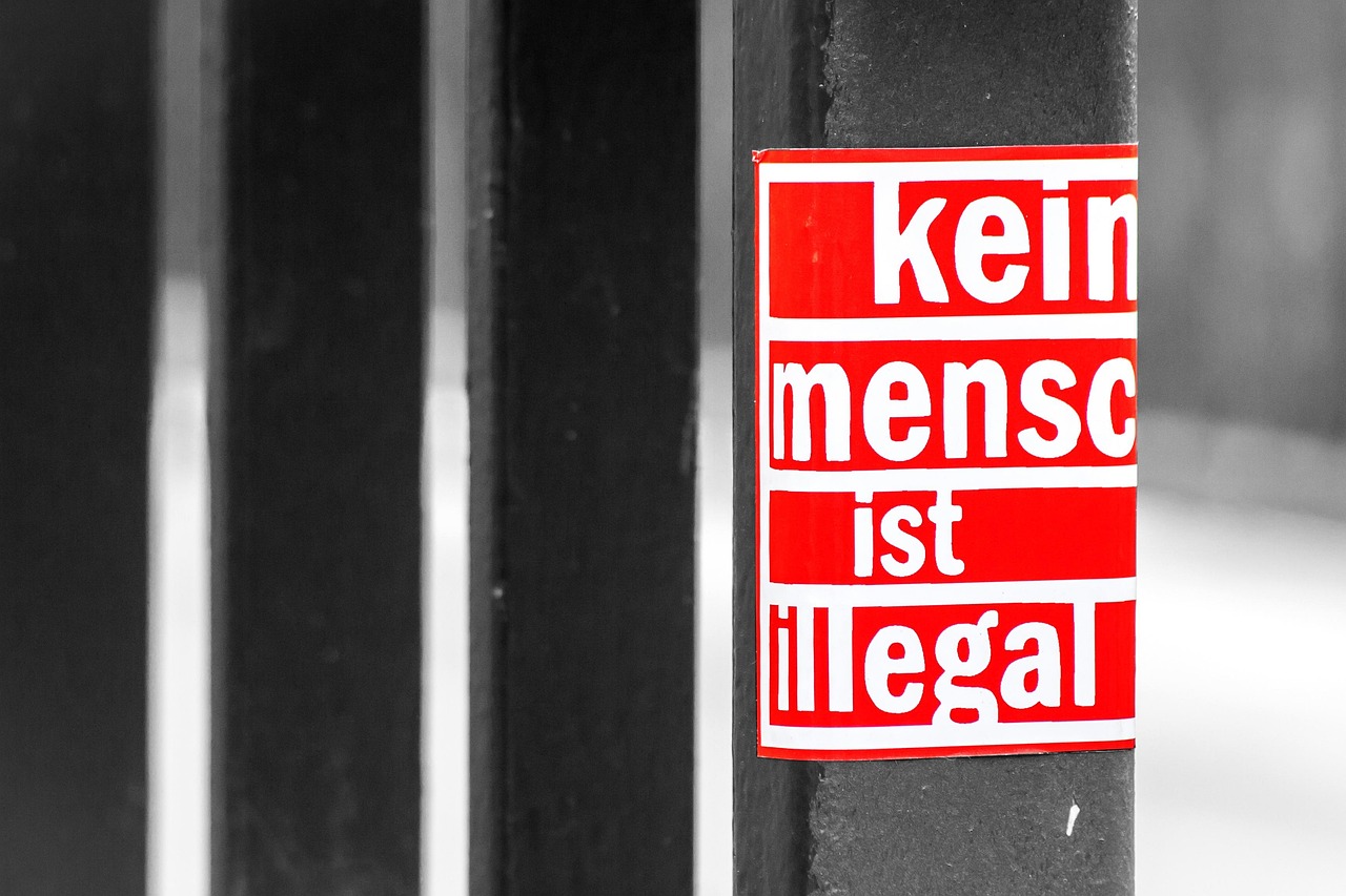 Napis 'Kein Mensch ist illegal' na czerwonej naklejce, symbolizuje sprzeciw wobec nielegalności ludzi.