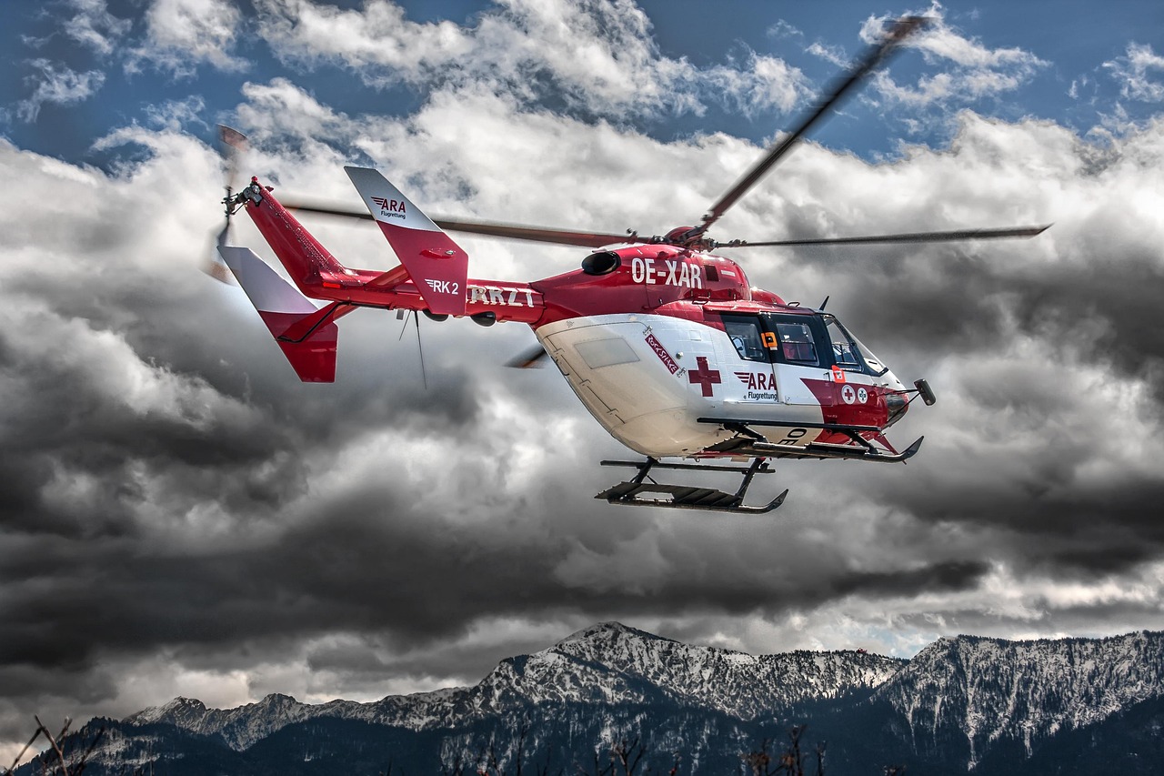Czerwono-biały helikopter ratowniczy latający na tle burzowych chmur i gór.