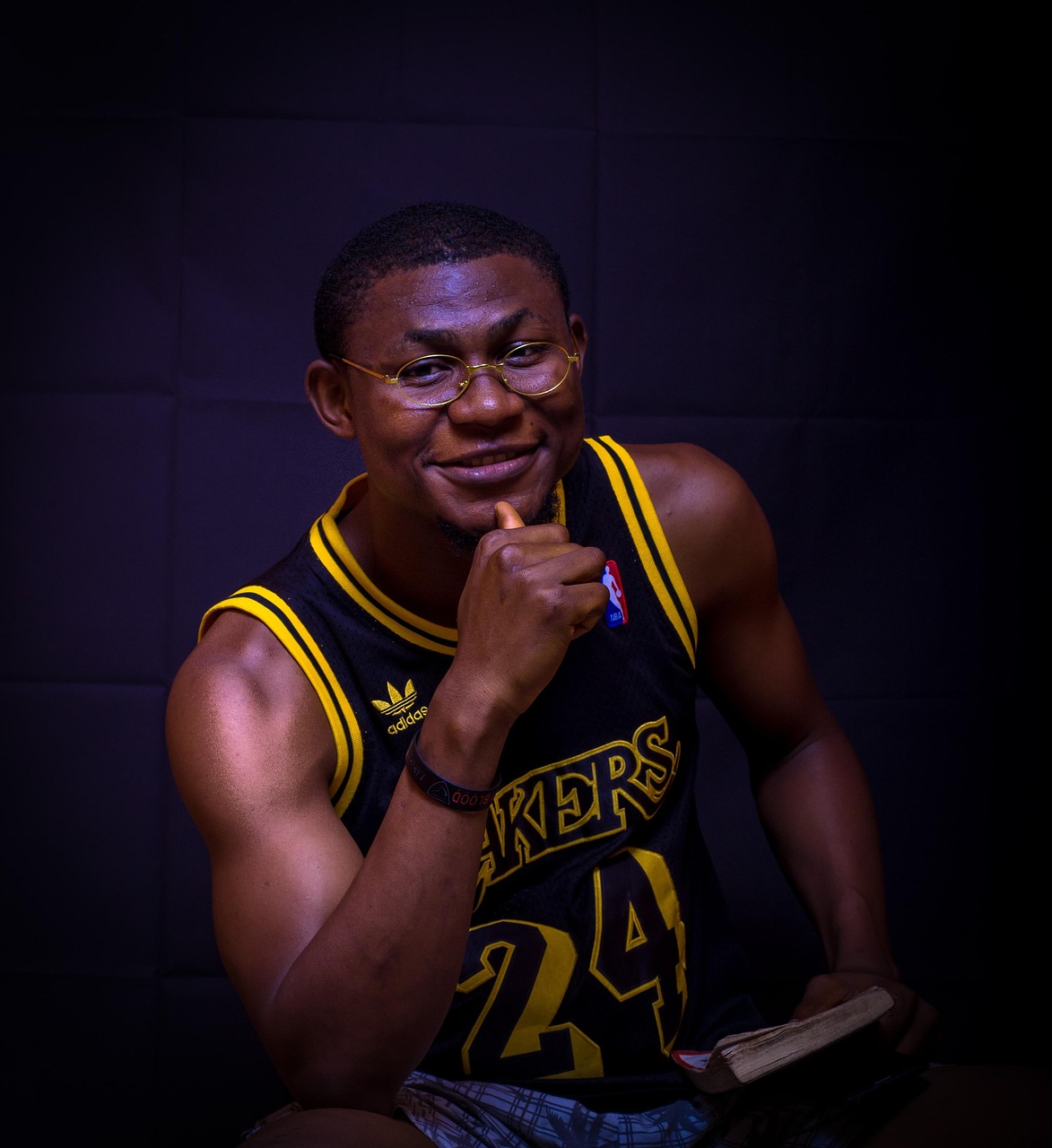 Młody mężczyzna w koszulce Lakers z numerem 24, w okularach, z książką.