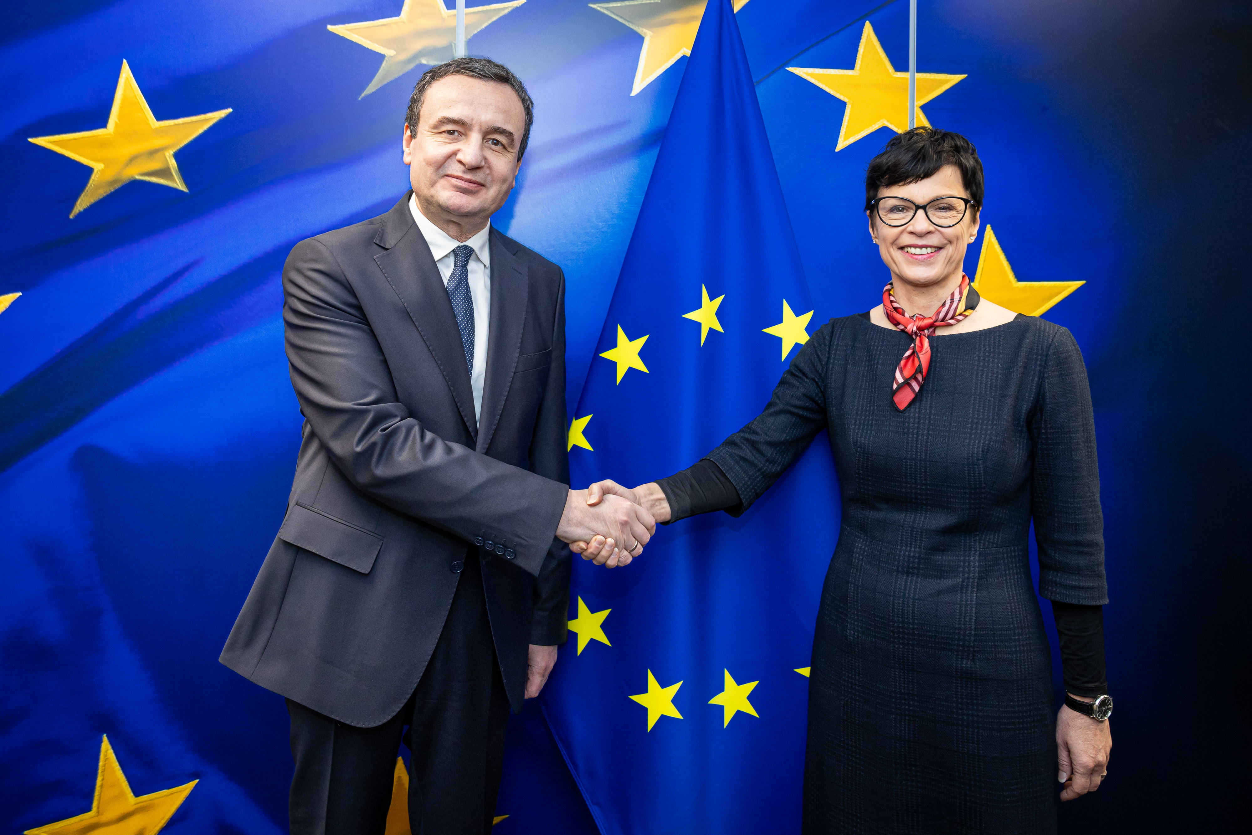 Albin Kurti, premier Kosowa, ściska dłoń z przedstawicielką UE na tle flagi UE, podkreślając napięcia i oskarżenia o ingerencję w wybory.