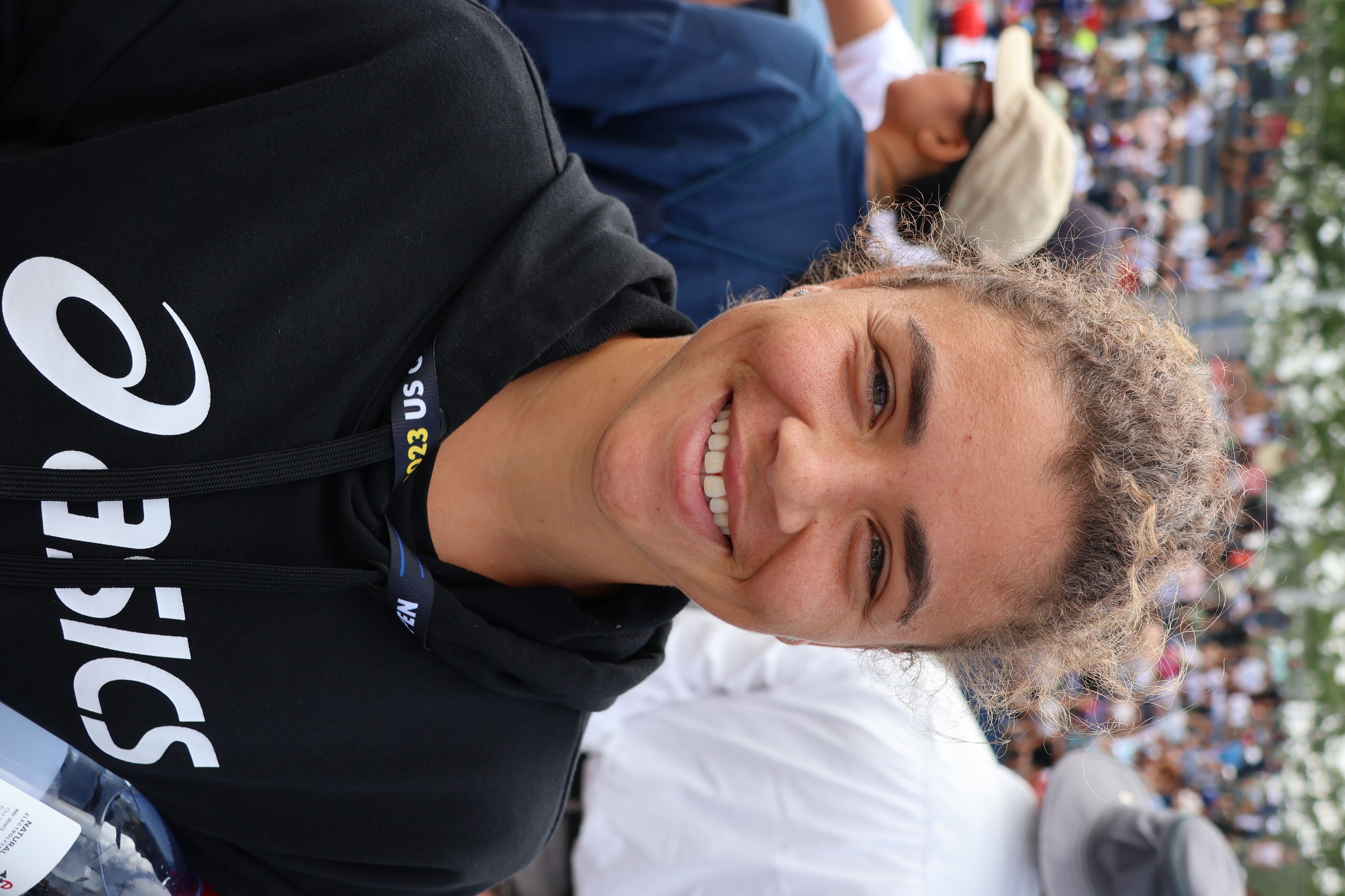 Jasmine Paolini uśmiecha się na korcie w Wuhan, ubrana w bluzę z kapturem z logo Asics.