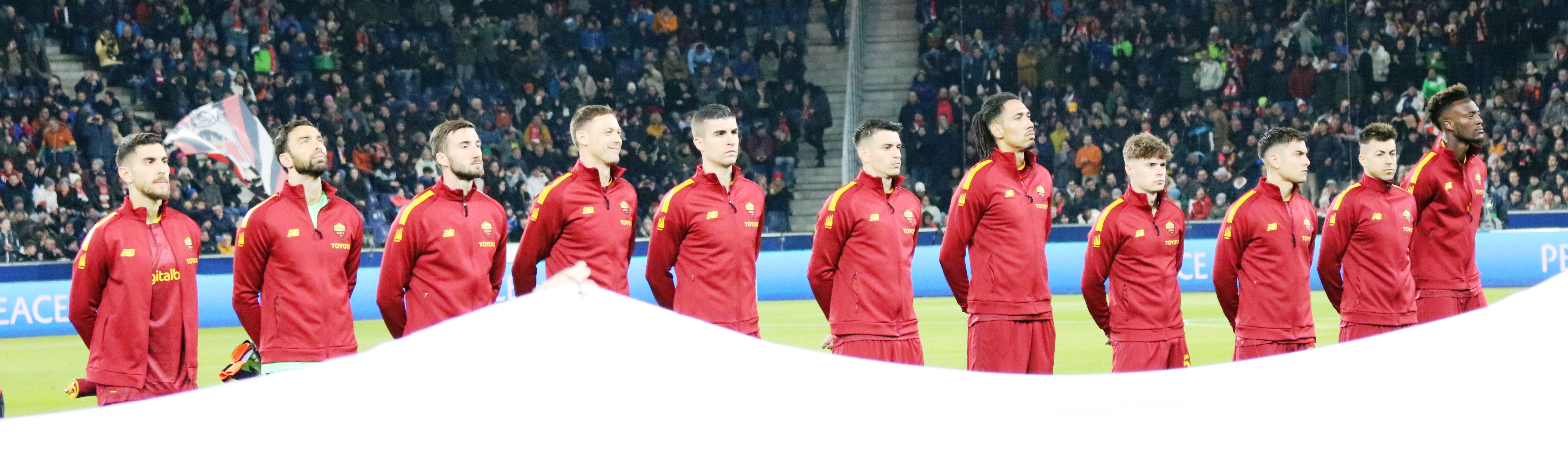 Piłkarze AS Roma w czerwonych strojach stoją w rzędzie na boisku.