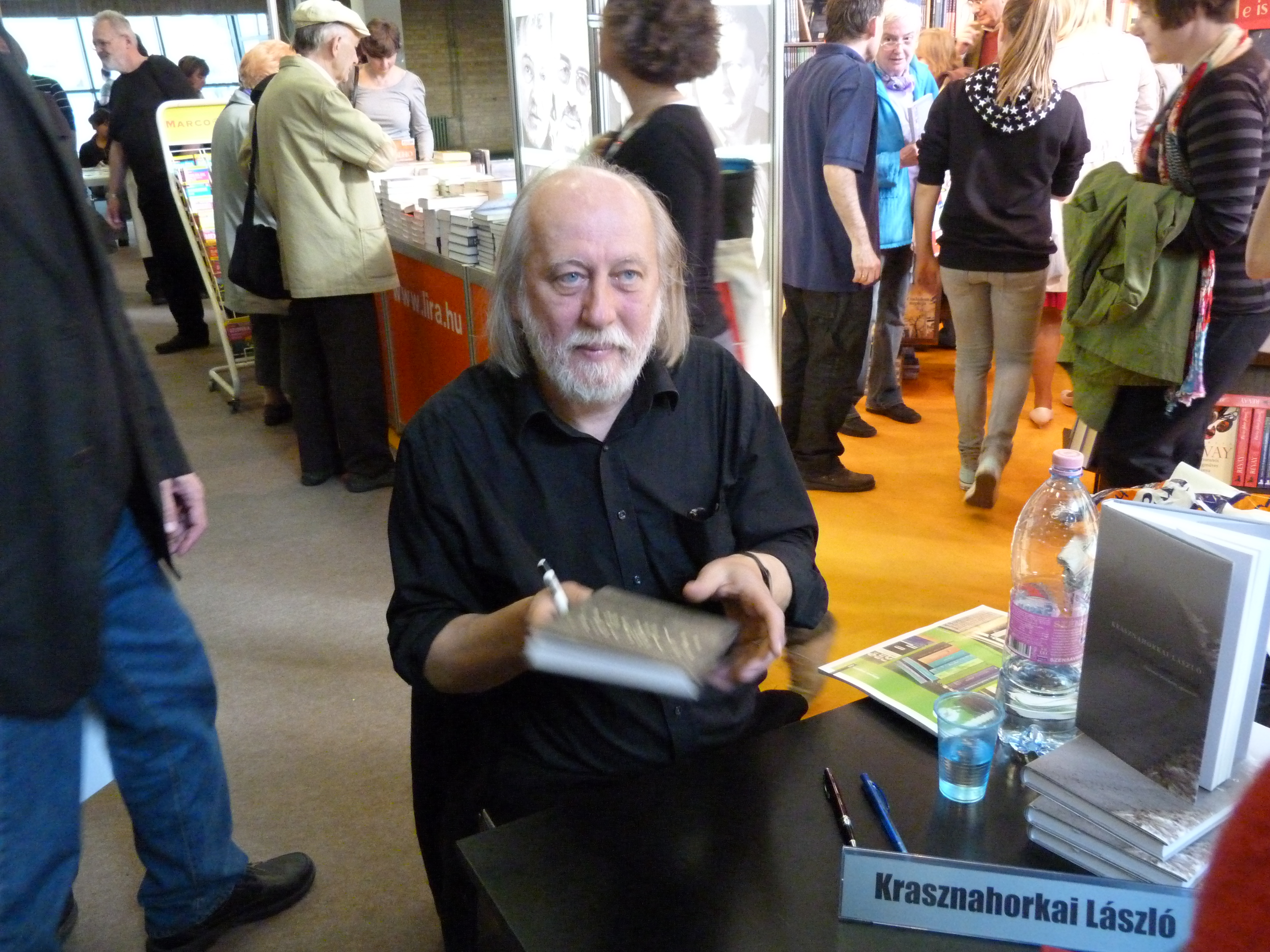 László Krasznahorkai, laureat Literackiej Nagrody Nobla, podpisuje książkę w otoczeniu czytelników.