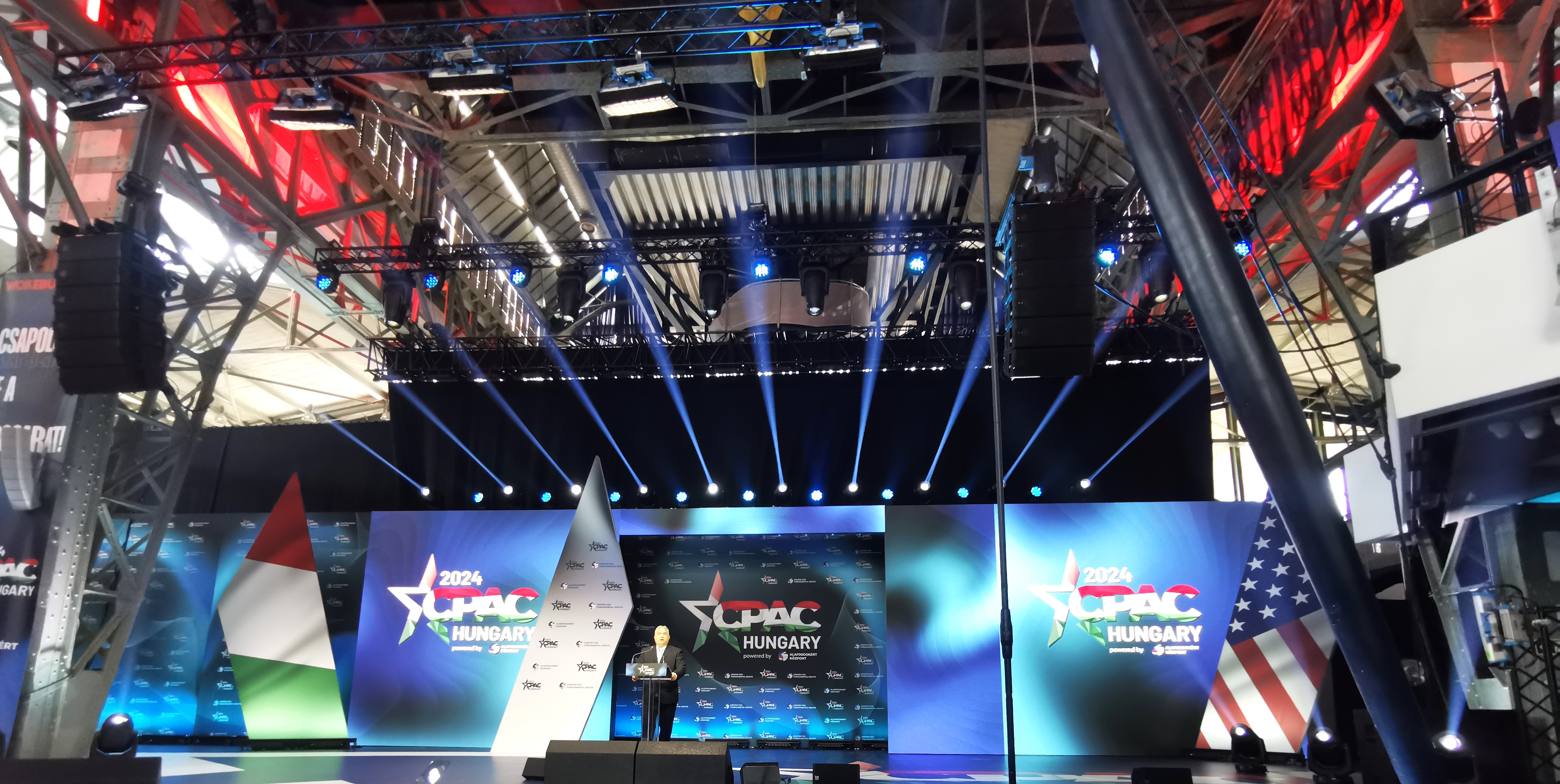 Viktor Orbán przemawia na scenie CPAC Hungary 2024, z flagami Węgier i USA w tle.