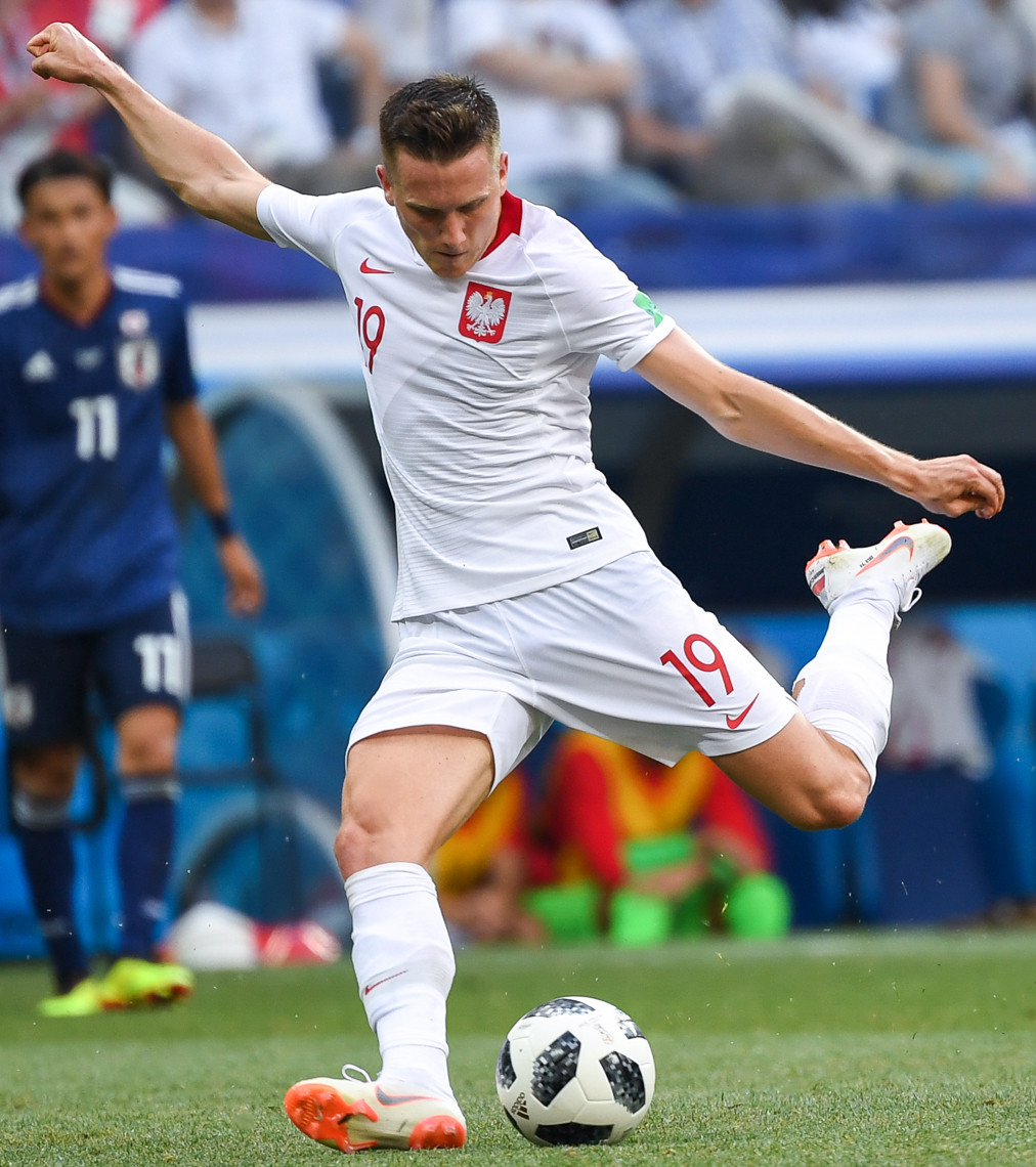 Piotr Zieliński w białej koszulce reprezentacji Polski kopie piłkę.