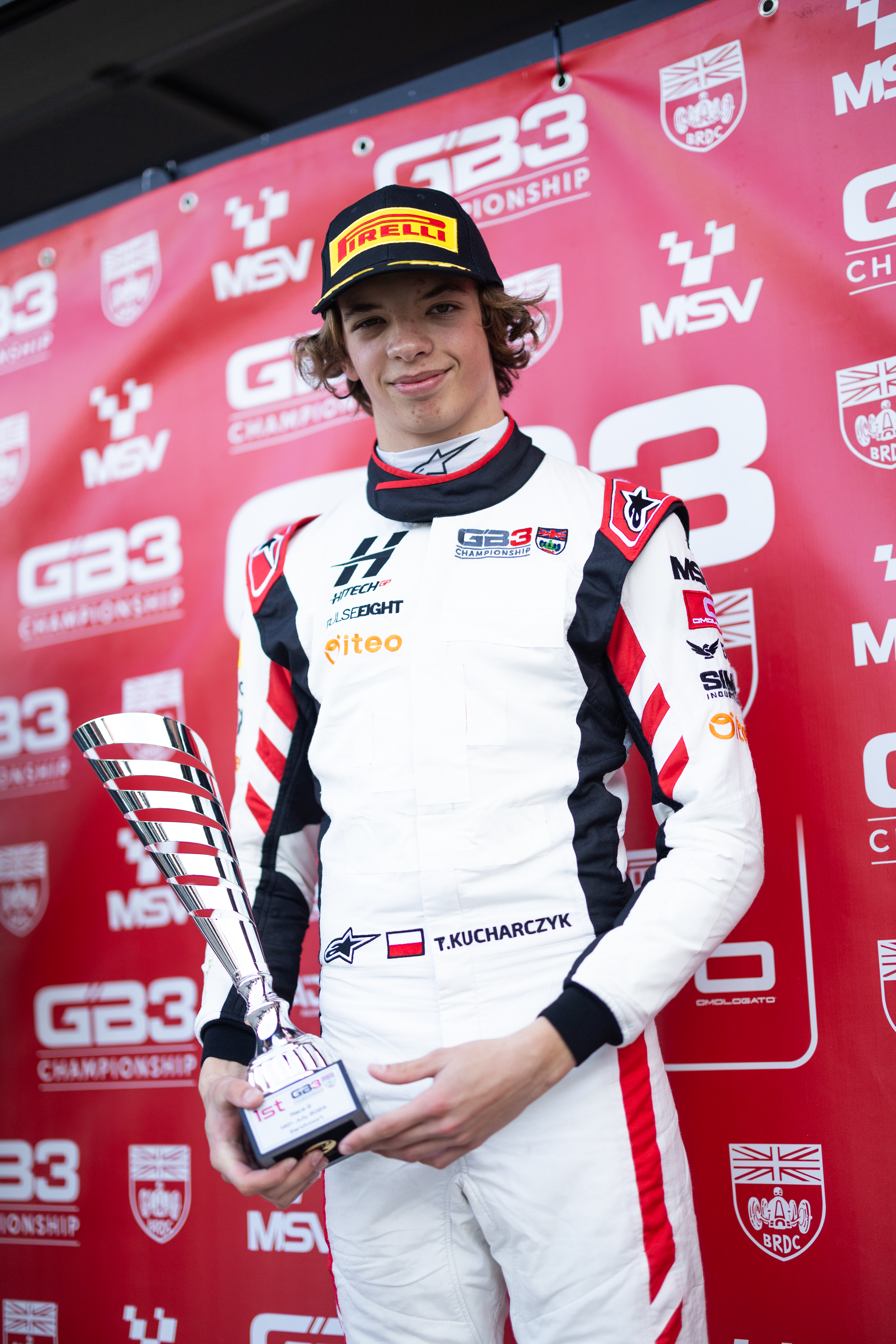 Tymoteusz Kucharczyk z pucharem, polski talent motorsportu, na tle banerów GB3 Championship.