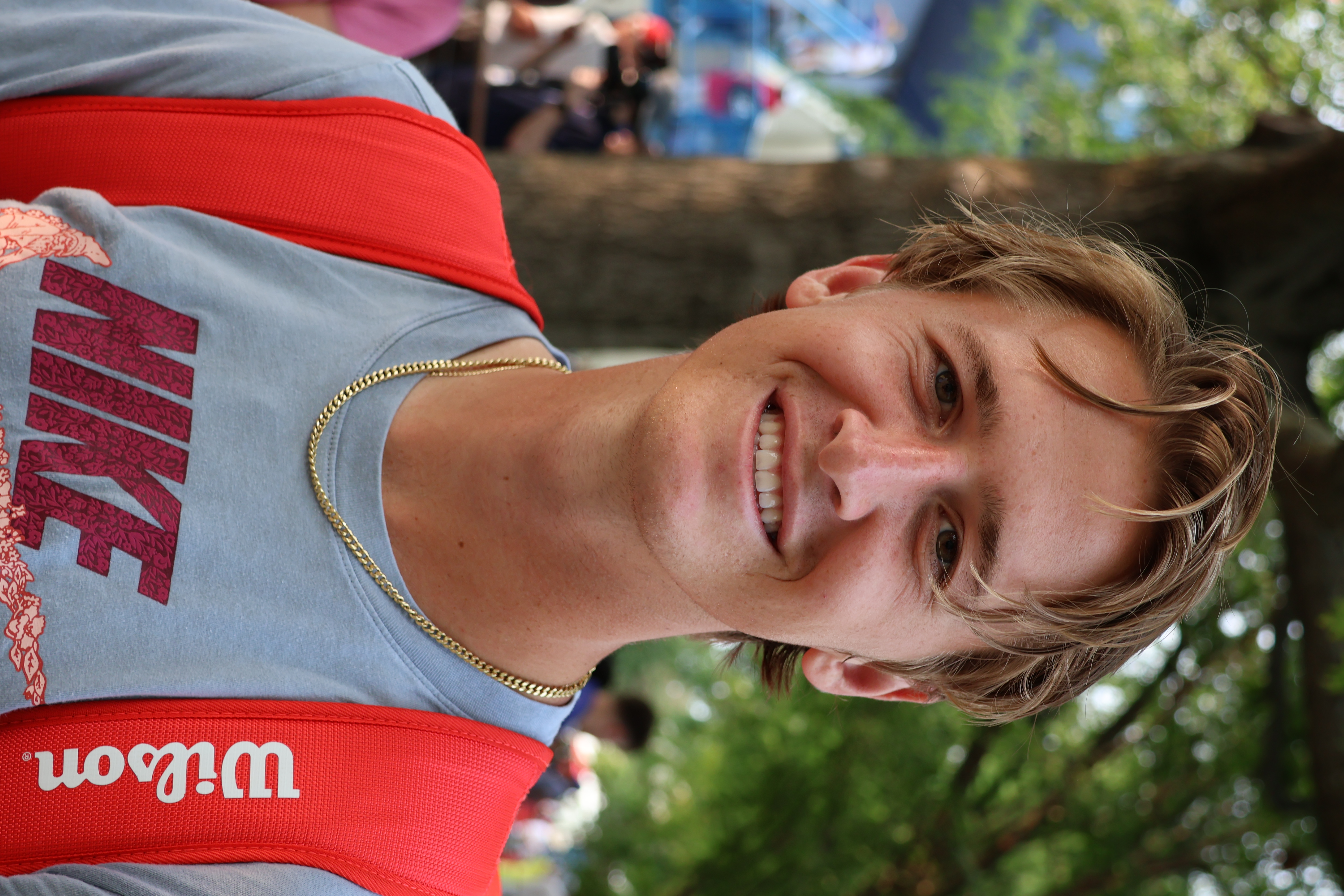 Sebastian Korda, syn legendy tenisa, w koszulce Nike i z czerwonym plecakiem, uśmiecha się do kamery.
